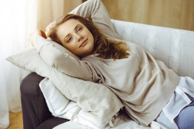 Mutlu esmer kadın ellerini başının arkasına koyuyor koltuğa yaslanıyor, Avrupalı kadın esniyor ve tembel haftasonunun keyfini çıkarıyor ya da sıcak oturma odasında tatilin tadını çıkarıyor.