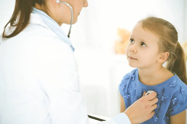 Doctor examinando a un niño por estetoscopio. Feliz niña sonriente paciente vestida con vestido azul es en la inspección médica habitual. Concepto de medicina — Foto de Stock