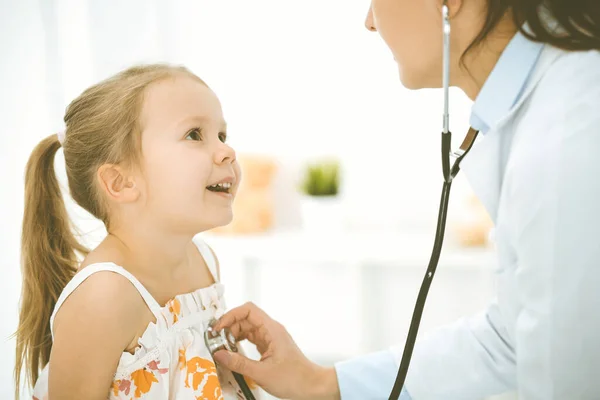 Bir çocuğu steteskopla muayene eden bir doktor. Parlak renkli elbise giymiş mutlu gülümseyen kız hasta her zamanki sağlık kontrolünde. — Stok fotoğraf