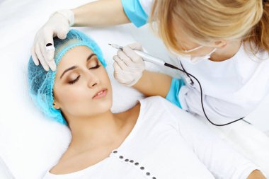 Kadın yüzüne kaş dövmesi yapan profesyonel bir güzellik uzmanı. Güzellik salonunda kalıcı kaş makyajı, yakın çekim. Kozmetoloji tedavisi