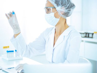 Koruyucu gözlüklü profesyonel kadın bilim adamı labaratuvarda mavi renkte reaksiyonlarla araştırma tüpü kullanıyor. Tıp ve bilim araştırmaları kavramları