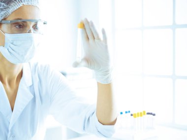 Koruyucu gözlüklü profesyonel kadın bilim adamı labaratuvarda mavi renkte reaksiyonlarla araştırma tüpü kullanıyor. Tıp ve bilim araştırmaları kavramları