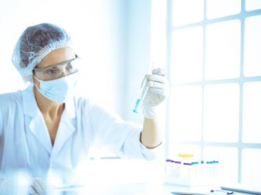 Koruyucu gözlüklü profesyonel kadın bilim adamı labaratuvarda mavi renkte reaksiyonlarla araştırma tüpü kullanıyor. Tıp ve bilim araştırmaları kavramları