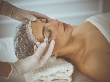 Güzellik uzmanı, genç esmer kadının yüzüne şırıngayla güzellik prosedürü uyguluyor. Kozmetik ilaç ve ameliyat, güzellik iğneleri.