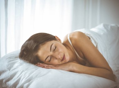 Güzel, genç, esmer kadın yatakta rahat ve mutlu bir şekilde yatarken uyuyor. Günaydın konsept.
