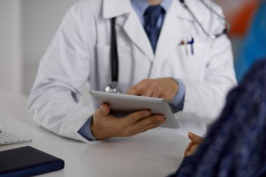 Bilinmeyen sakallı doktor ve hasta kadın tablet bilgisayarı kullanırken sağlık muayenesini tartışıyorlar, yakın plan. Tıp konsepti