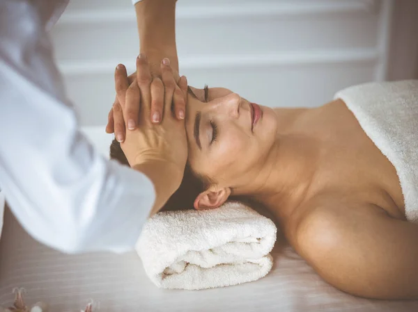 Beautiful brunette woman enjoying facial massage with closed eyes comfortable and blissful. Relaxing treatment in medicine and spa center concepts — 스톡 사진