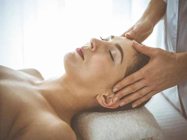 Beautiful brunette woman enjoying facial massage with closed eyes comfortable and blissful. Relaxing treatment in medicine and spa center concepts — 스톡 사진