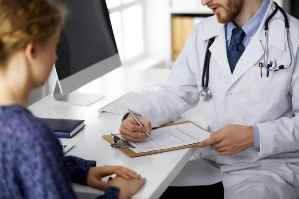 Unknown bearded doctor and patient woman discussing current health examination while sitting in sunny clinic, close-up. Medicine concept — Stock Photo, Image