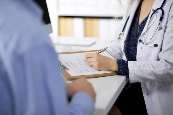 Kadın doktor ve erkek hasta klinikte otururken sağlık muayenesini tartışıyorlar. — Stok fotoğraf