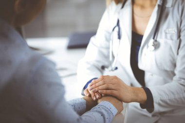 Bilinmeyen kadın-doktor, klinikteki dolapta yan yana otururken hastaya güven vermek için hastasının elini tutuyor ve mevcut sağlık muayenesini tartışıyor. Kadın.