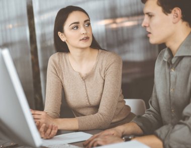 Yeşil gömlekli arkadaş canlısı genç işadamı ve programcı, modern bir ofiste masa başında bayan bir meslektaşla birlikte otururken bilgisayar üzerinde çalışıyor. Kadınlara odaklan. Başarılı olma kavramı
