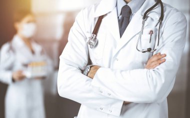 Güneşli klinikte kolları çapraz duran koruyucu maskeli kimliği belirsiz erkek doktor. Coronavirüs salgını sırasında ilaç kavramı