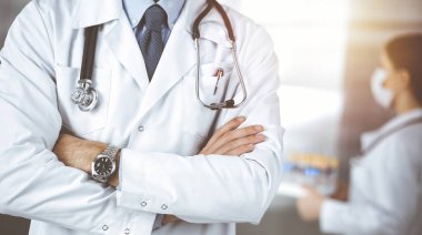 Güneşli klinikte kolları çapraz duran koruyucu maskeli kimliği belirsiz erkek doktor. Coronavirüs salgını sırasında ilaç kavramı