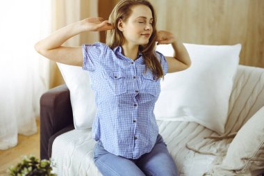 Mutlu sarışın kadın ellerini başının arkasına koyuyor koltuğa yaslanmış beyaz kadın tembelce haftasonunun ya da güneşli oturma odasında tatilin tadını çıkarıyor.