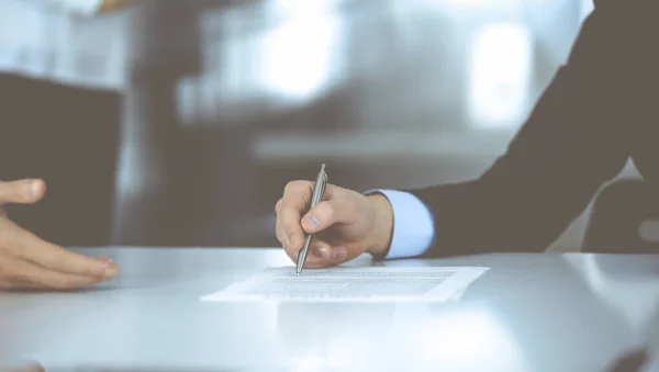 Gente de negocios discutiendo un contrato en la reunión o negociación, sentados en el escritorio juntos, y una mujer desconocida en el fondo, de cerca. Grupo de empresarios desconocidos en una oficina moderna — Foto de Stock