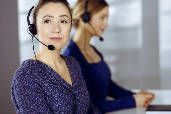 Deux femmes d'affaires ont des conversations avec les clients par écouteurs, tout en étant assis au bureau dans un bureau moderne. Groupe de personnes diverses dans un centre d'appels. Télémarketing et service à la clientèle — Photo