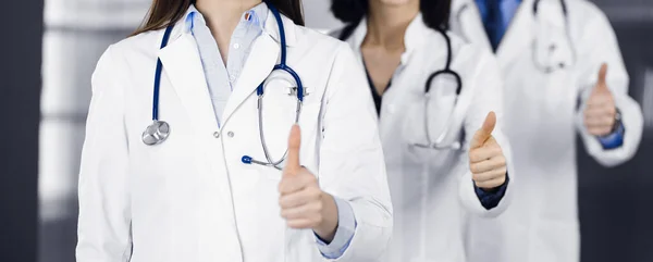 Group of doctors standing as a team with thumbs up in sunny clinic. Good news and Hope for a cure. Medicine concept during Coronavirus pandemic. Covid-2019 — Stock Photo, Image