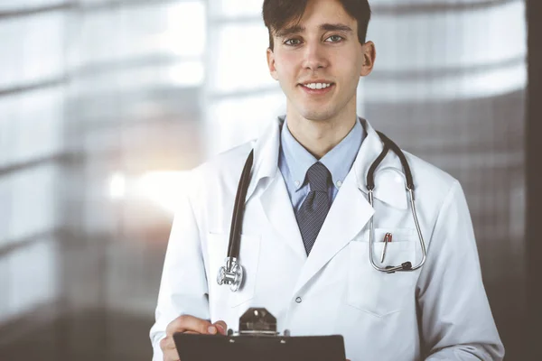 Дружелюбный молодой врач-мужчина, стоящий с планшетом в современной клинике. Концепция медицины — стоковое фото