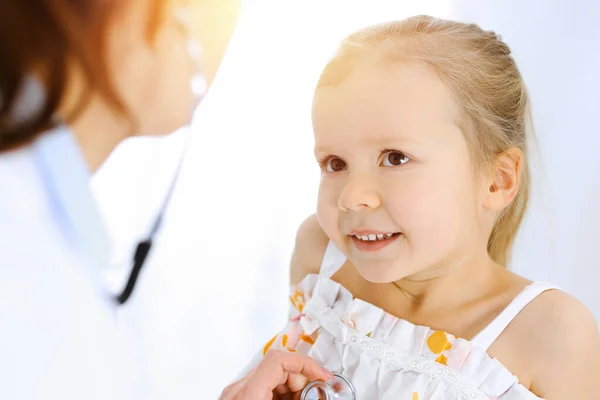 Doctor examinando a una niña por estetoscopio. Feliz niño sonriente paciente en la inspección médica habitual. Medicina y conceptos sanitarios — Foto de Stock