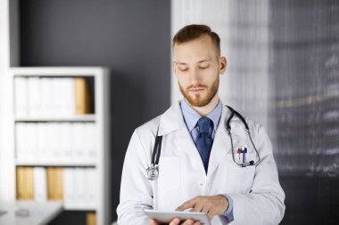 Klinikte tablet bilgisayar kullanan arkadaş canlısı kızıl sakallı doktor. Hastane ve tıp konseptinde mükemmel bir tıbbi hizmet.