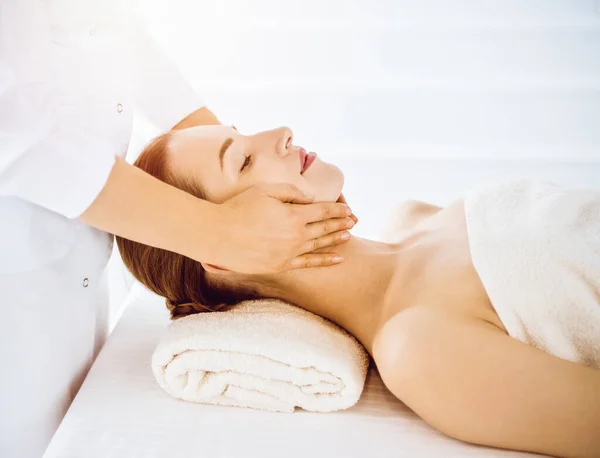 Красива жінка насолоджується масажем обличчя з закритими очима в сонячному спа-центрі — стокове фото