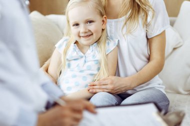 Doktor ve hasta. Pediyatrist, annesiyle birlikte küçük kızı muayene ederken pano kullanıyor. Sağlık muayenesinde mutlu beyaz çocuk. Tıp konsepti