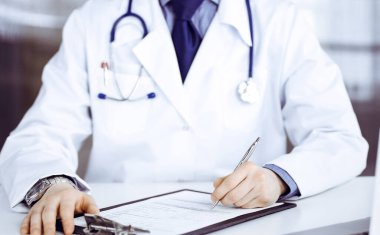 Bilinmeyen erkek doktor, klinikte, yakın planda pano ile oturuyor ve çalışıyor. İşteki genç doktor. Mükemmel sağlık hizmeti, tıp konsepti