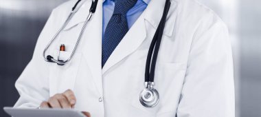 Klinikte dururken elinde tablet bilgisayar tutan kimliği belirsiz bir erkek doktor. Coronavirüs salgını sırasında ilaç kavramı