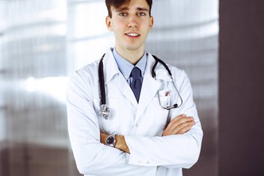 Klinikte kolları kavuşturulmuş gülümseyen adam-doktor. Hastanede genç ve zeki bir doktorla mükemmel bir tıbbi hizmet. Tıp konsepti