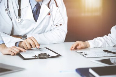 Bilinmeyen bir grup doktor masanın başında oturmuş güneşli hastane ofisinde hastalıkların tedavisini tartışıyorlar. Covid 2019