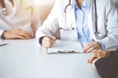 Erkek meslektaşı olan bilinmeyen kadın-doktor güneşli klinikteki masada otururken hastaya danışıyor, yakın plan. Covid 2019