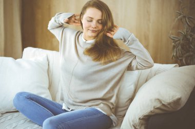 Mutlu esmer kadın ellerini başının arkasına koyuyor koltuğa yaslanıyor Avrupalı kadın tembel hafta sonunun keyfini çıkarıyor ya da sıcak oturma odasında tatilin tadını çıkarıyor, ev hanımı ev işi yaptıktan sonra rahatlıyor.