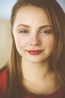 Zeki, kendinden emin, gülümseyen, Avrupalı bir kadının kollarını kavuşturup evinde dikilirken çekilmiş bir fotoğrafı. Çekici genç kız öğrenci serbest çalışan, kırmızı giyinmiş, kameraya bakıyor.