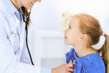 Doktor steteskopla küçük bir kızı muayene ediyor. Her zamanki tıbbi muayenede gülümseyen çocuk hasta. Tıp ve sağlık hizmetleri kavramları