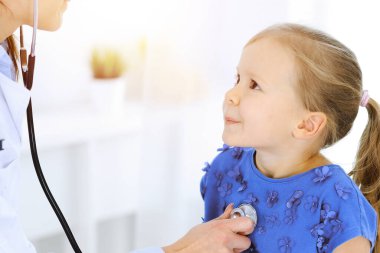 Doktor steteskopla küçük bir kızı muayene ediyor. Her zamanki tıbbi muayenede gülümseyen çocuk hasta. Tıp ve sağlık hizmetleri kavramları