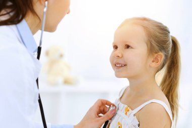 Doktor steteskopla küçük bir kızı muayene ediyor. Her zamanki tıbbi muayenede gülümseyen çocuk hasta. Tıp ve sağlık hizmetleri kavramları