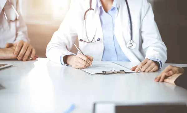 Mulher-médico desconhecido com colega do sexo masculino estão consultando mulher paciente enquanto sentado na mesa na clínica ensolarada, close-up. Covid 2019 — Fotografia de Stock