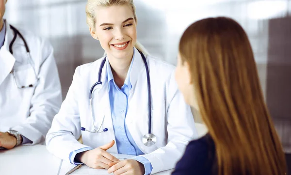 Ärztin und männlicher Kollege beraten die Patientin, während sie am Schreibtisch in der modernen Klinik sitzen. Perfekter medizinischer Service, medizinisches Konzept — Stockfoto