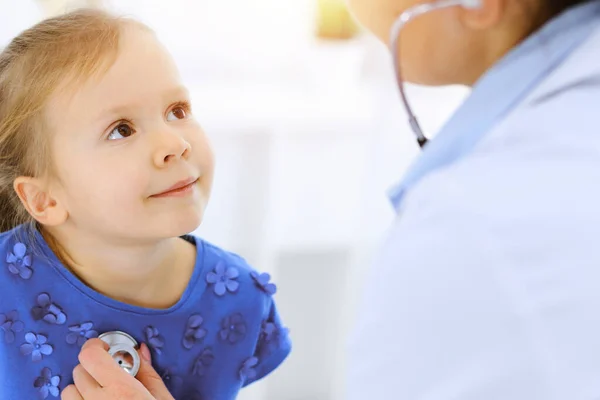 Arzt untersucht ein kleines Mädchen per Stethoskop. Glücklich lächelnder Kinderpatient bei der üblichen ärztlichen Untersuchung. Medizin- und Gesundheitskonzepte — Stockfoto