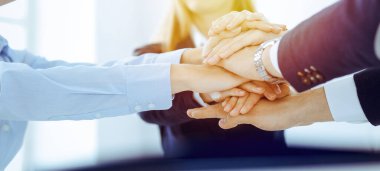 İş dünyası ekibi güneşli ofiste ellerini birleştiriyor. El ele tutuşan ve arkadaşlık ve takım çalışması kavramını temsil eden bir grup insan