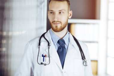 Güneşli klinikte duran dost canlısı sakallı doktor. Hekim portresi. Tıp konsepti