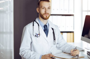 Dost canlısı sakallı doktor güneşli klinikteki panoda oturuyor ve yazıyor. Tıp konsepti