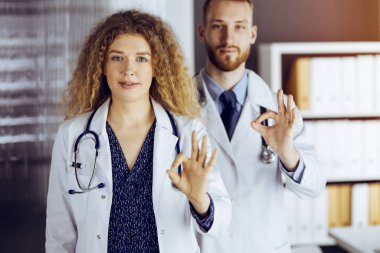 Hastane ofisinde baş parmakları havada iki doktor. Tıbbi yardım, viral enfeksiyon ve tıp konseptiyle mücadele
