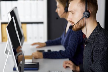 Modern ofiste otururken kulaklıkla konuşan sakallı iş adamı. Çağrı merkezinde çeşitli insanlar var. Tele pazarlama ve müşteri hizmetleri