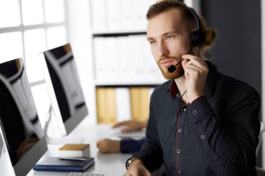 Modern ofiste otururken kulaklıkla konuşan sakallı iş adamı. Çağrı merkezinde çeşitli insanlar var. Tele pazarlama ve müşteri hizmetleri