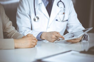 Bilinmeyen erkek doktor ve hasta kadın klinikte oturup tablet bilgisayar kullanırken bir şeyler tartışıyorlar. Hastanedeki en iyi sağlık hizmeti, ilaç, salgın durdurma.