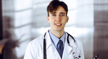 Modern klinikte dostane genç bir erkek doktor elinde bir panoyla dikiliyor. Bayan meslektaşım, doktorların arka planında ilaç kayıtları doldurmakla meşgul. Tıp konsepti