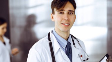 Modern klinikte dostane genç bir erkek doktor elinde bir panoyla dikiliyor. Bayan meslektaşım, doktorların arka planında ilaç kayıtları doldurmakla meşgul. Tıp konsepti