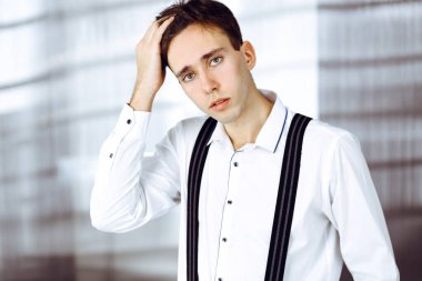 Modern ofiste beyaz gömlekli, dost canlısı genç bir işadamı duruyor.